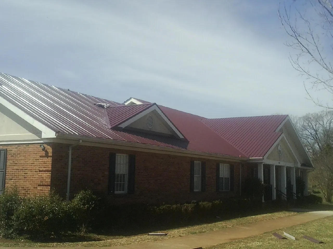 Red metal roof with gabled entries on a long brick building, from a Hail Damage Roof Repair job in Homer