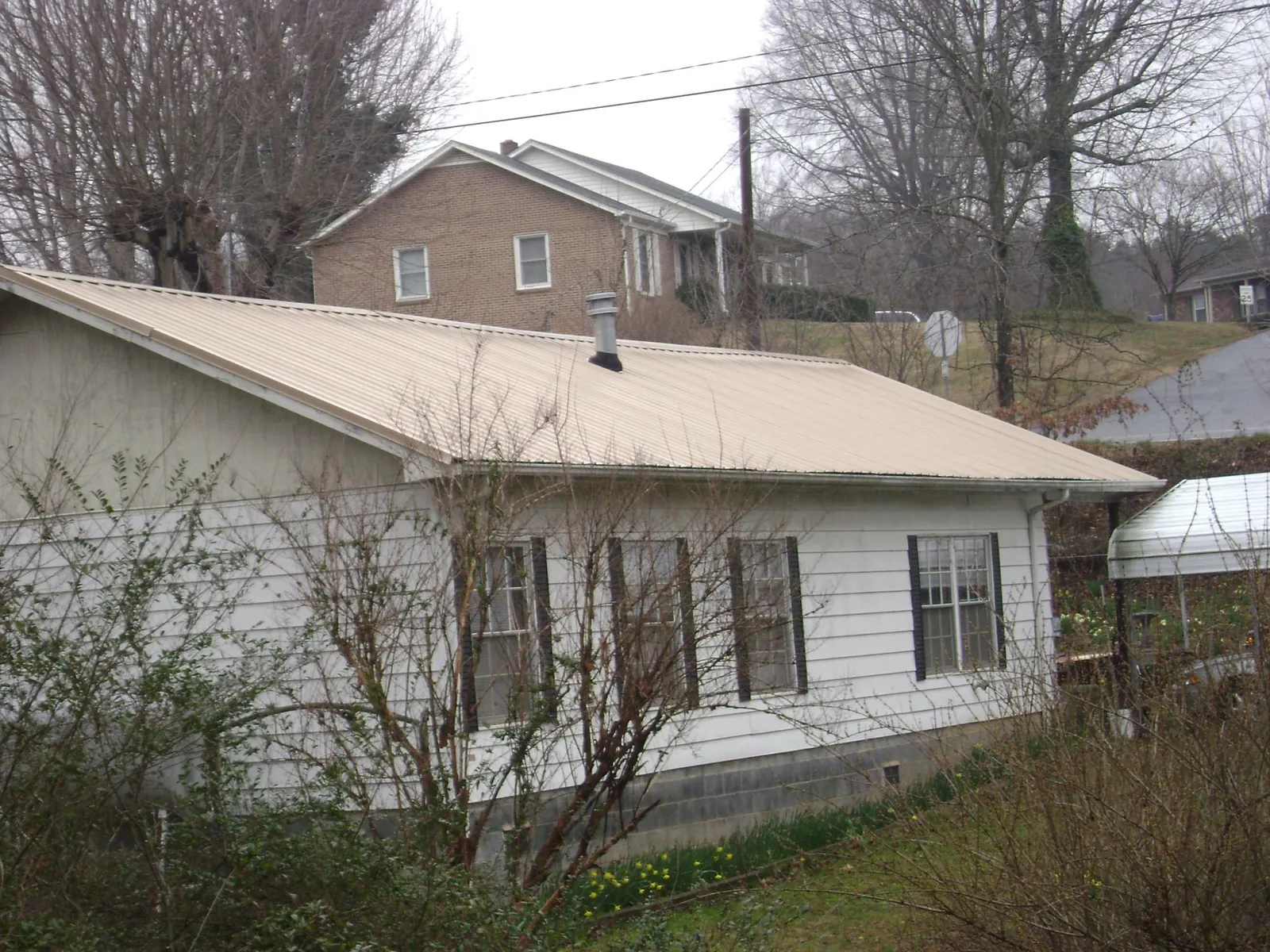 Tan metal roof on a white sided house set into a hillside — Commercial Roofing by Roofing Brothers in Homer